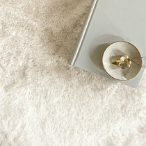 A gray book and a glass bowl with gold jewelry on a light, textured surface.