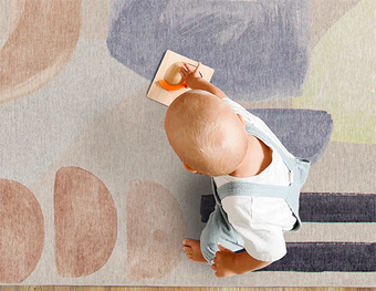 Baby playing with a wooden toy on a colorful abstract-patterned rug.