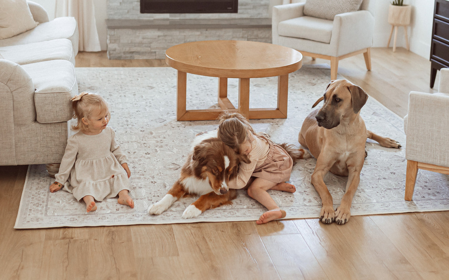 Two children sitting on a rug with two dogs in a cozy living room.