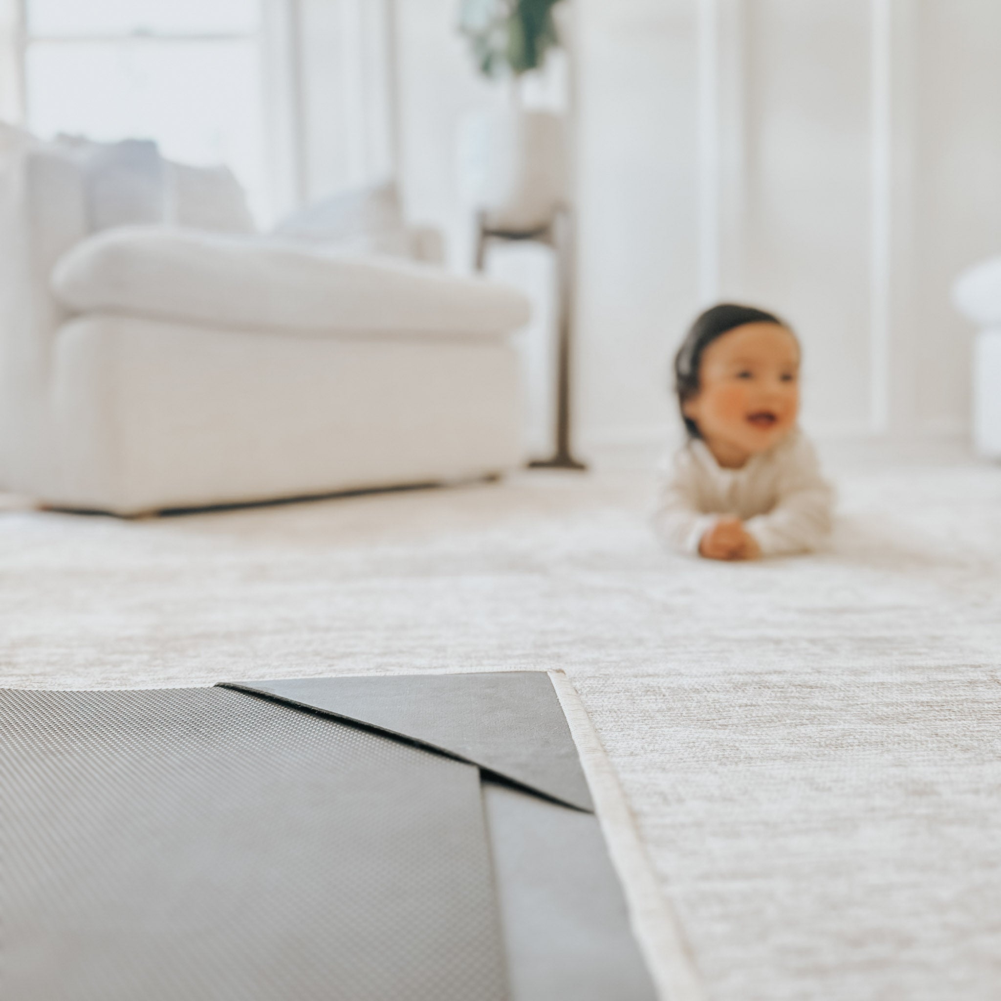A baby smiling and crawling on a soft rug in a bright living room.